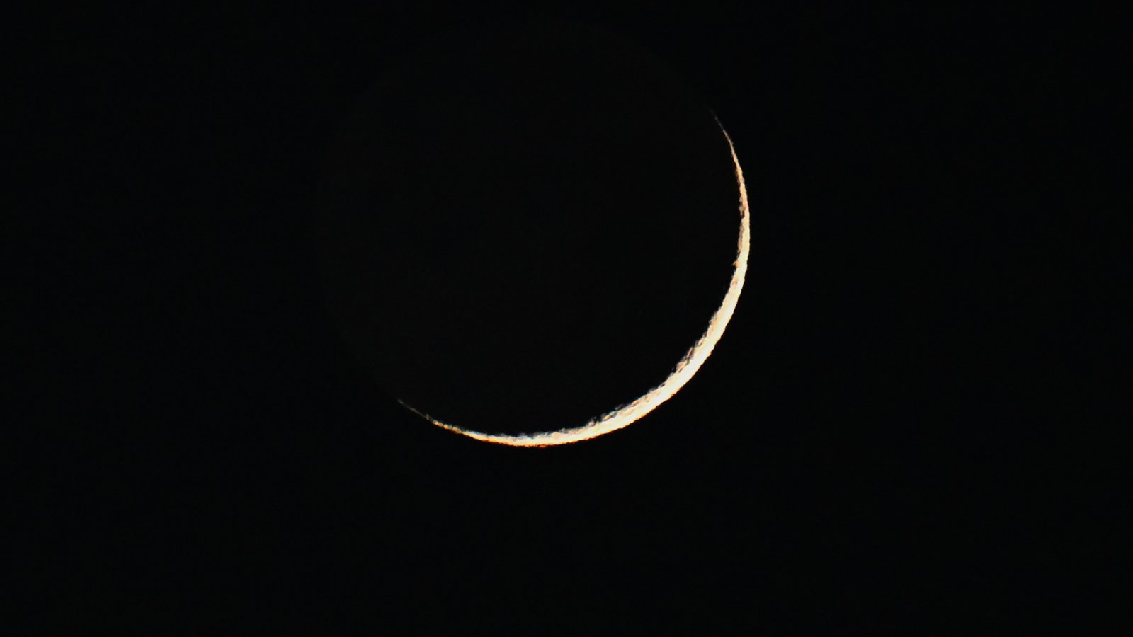 The thin crescent of the waxing moon is pictured against a dark sky.