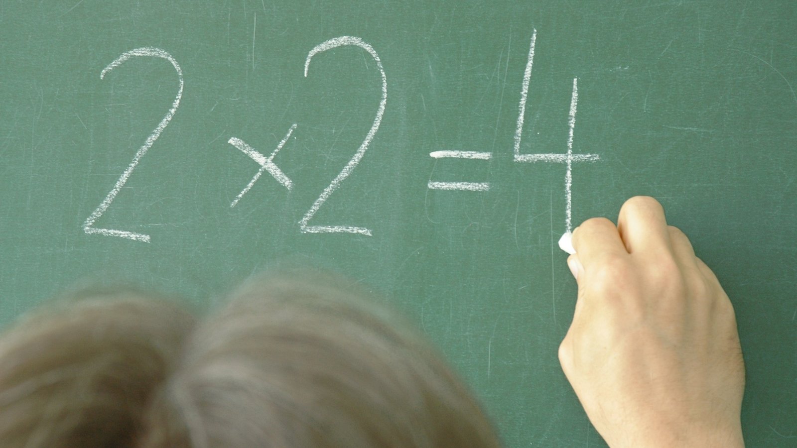 Hand writing 2+2=4 on chalkboard