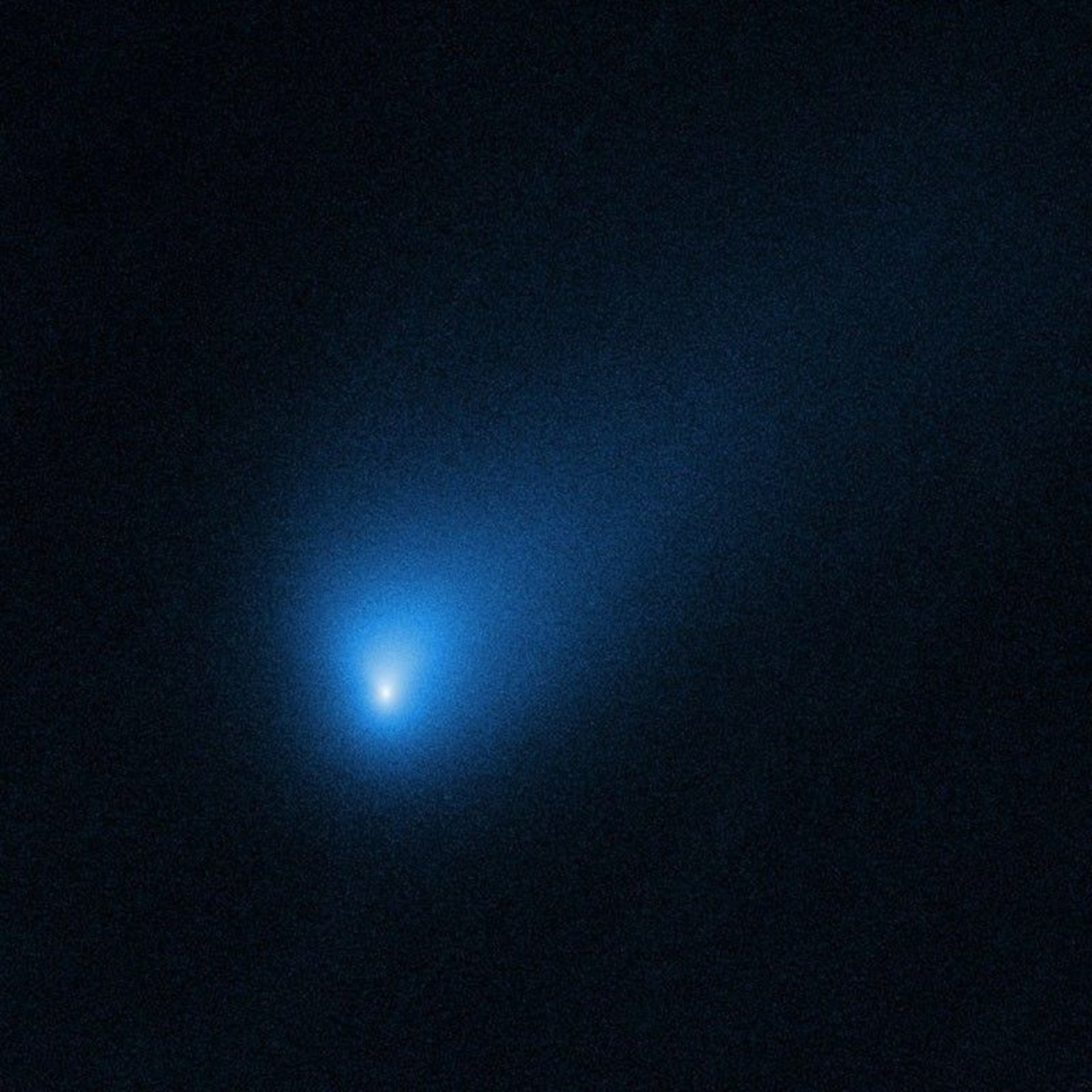 A blurry view of a blue, distant comet in space emitting a tail of debris