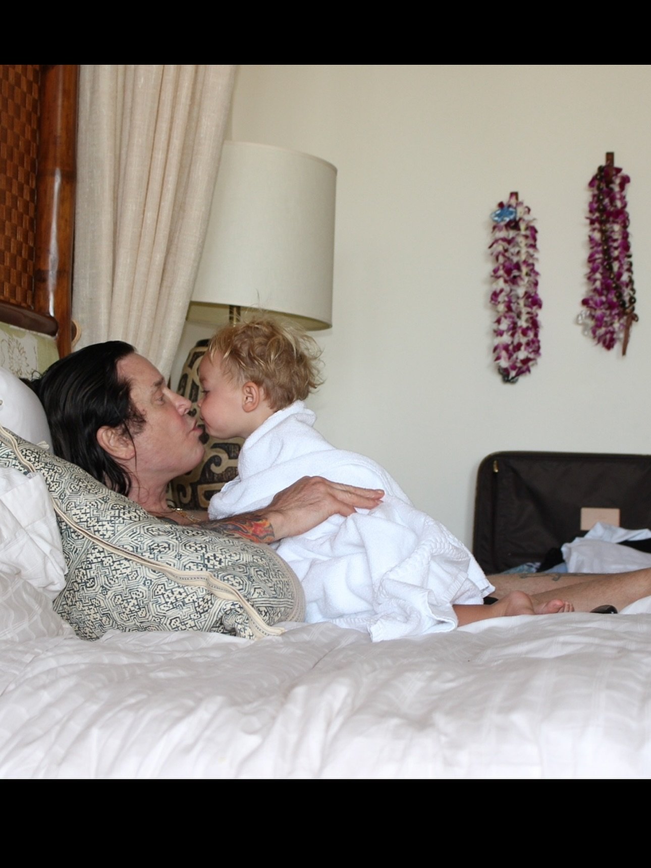 Ozzy Osbourne kisses a grandchild on a bed. 