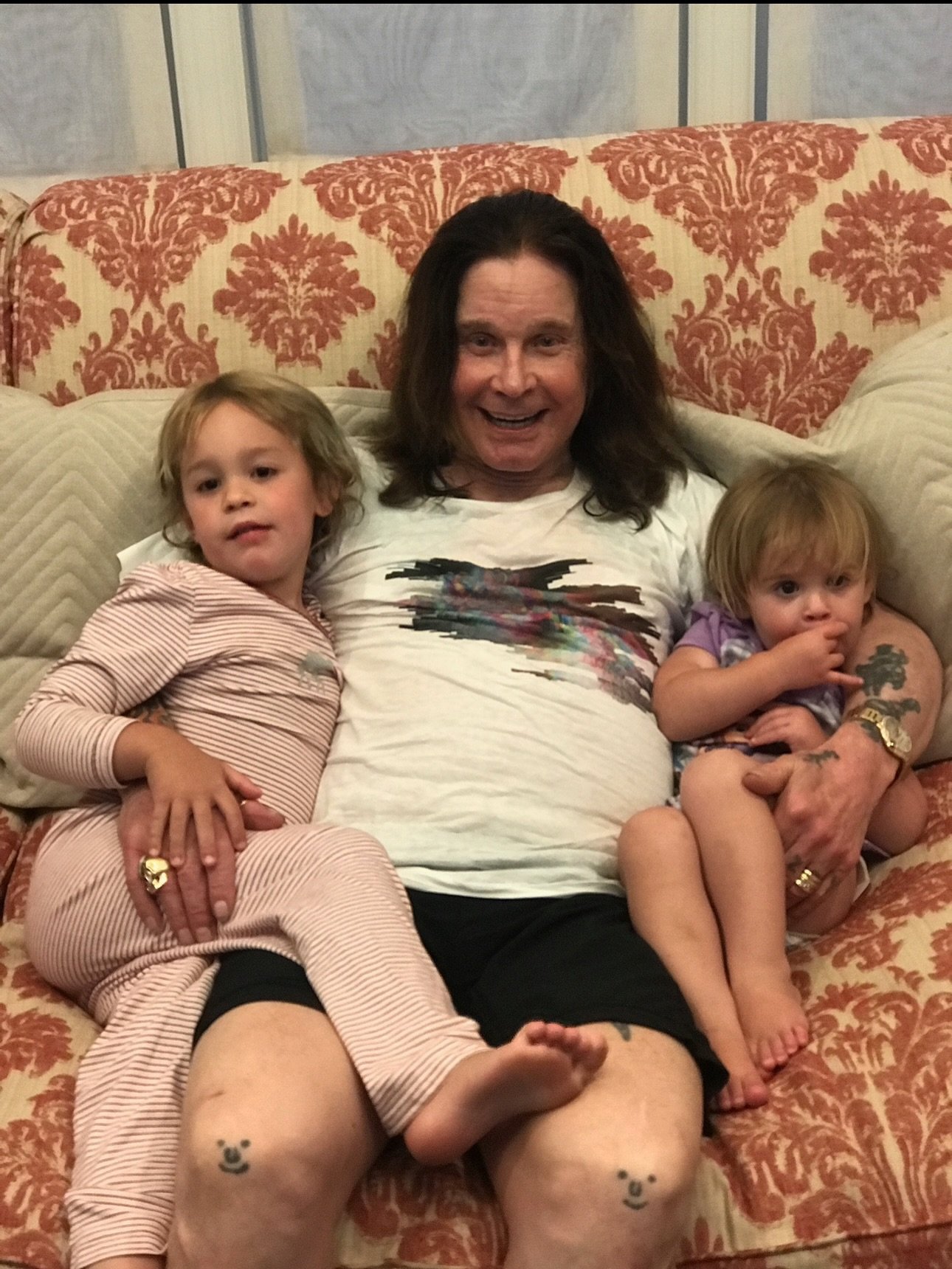 Ozzy Osbourne with two granddaughters on a couch. 