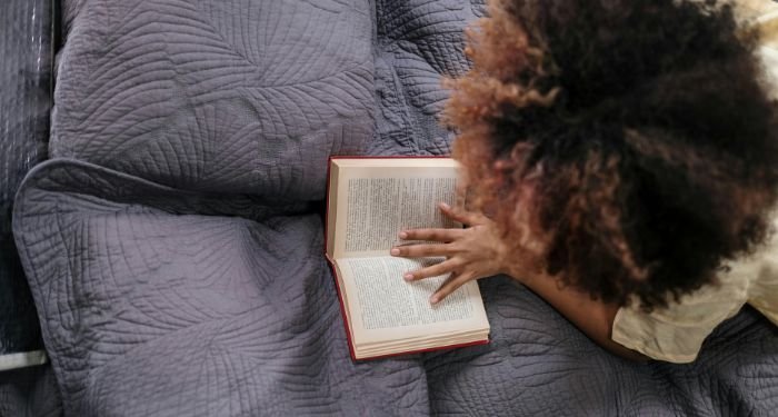 a tan-skinned person with a big afro lying on their tummy and reading a book
