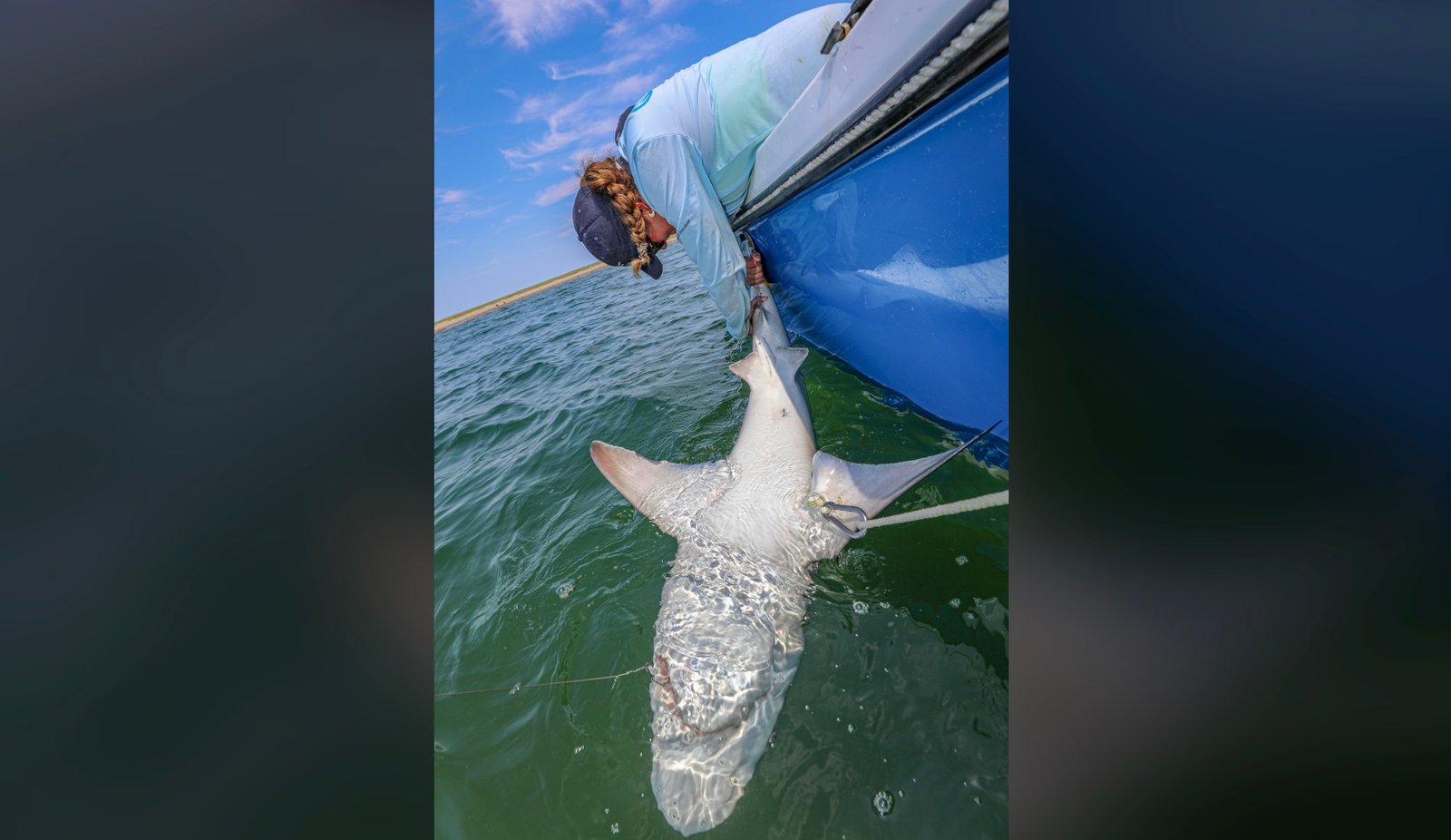 woman holding shark upside down next to a boat