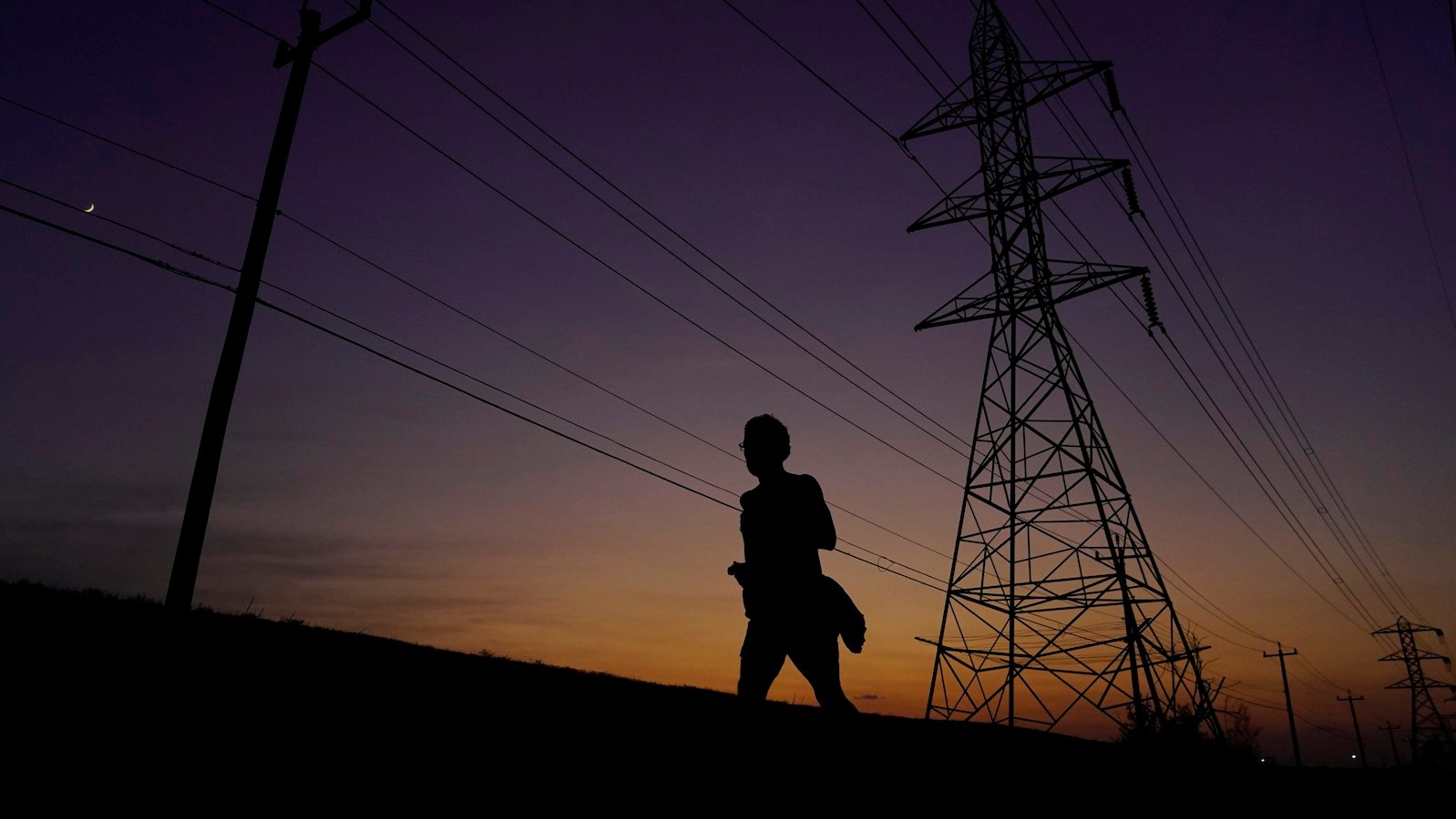 The silhoutte of a woman against the night sky and a power grid.