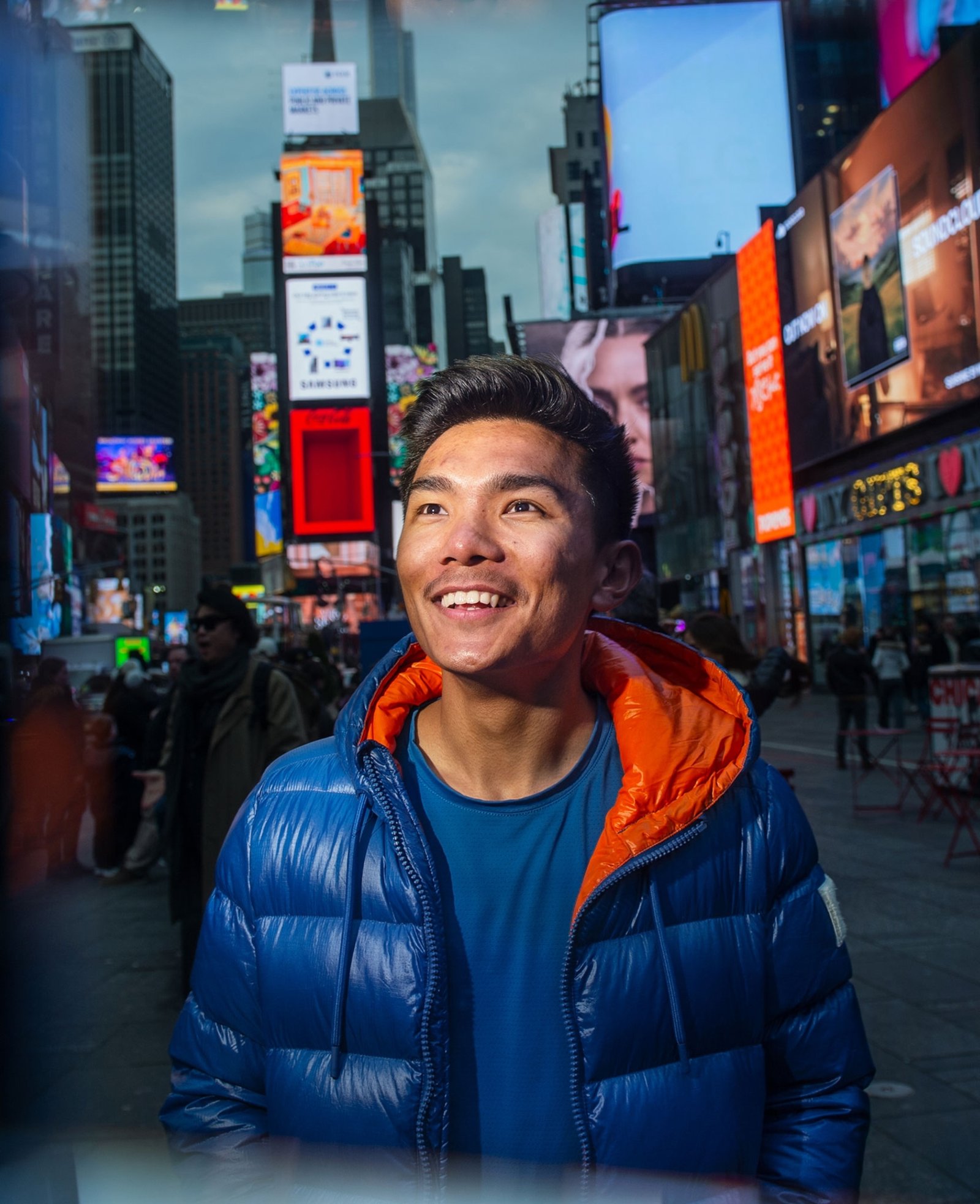 man in time square new york at night looking at lights smiling