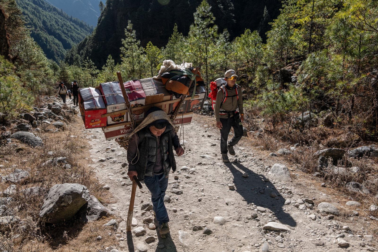 two men hiking up a hill one carrying a large pack of items