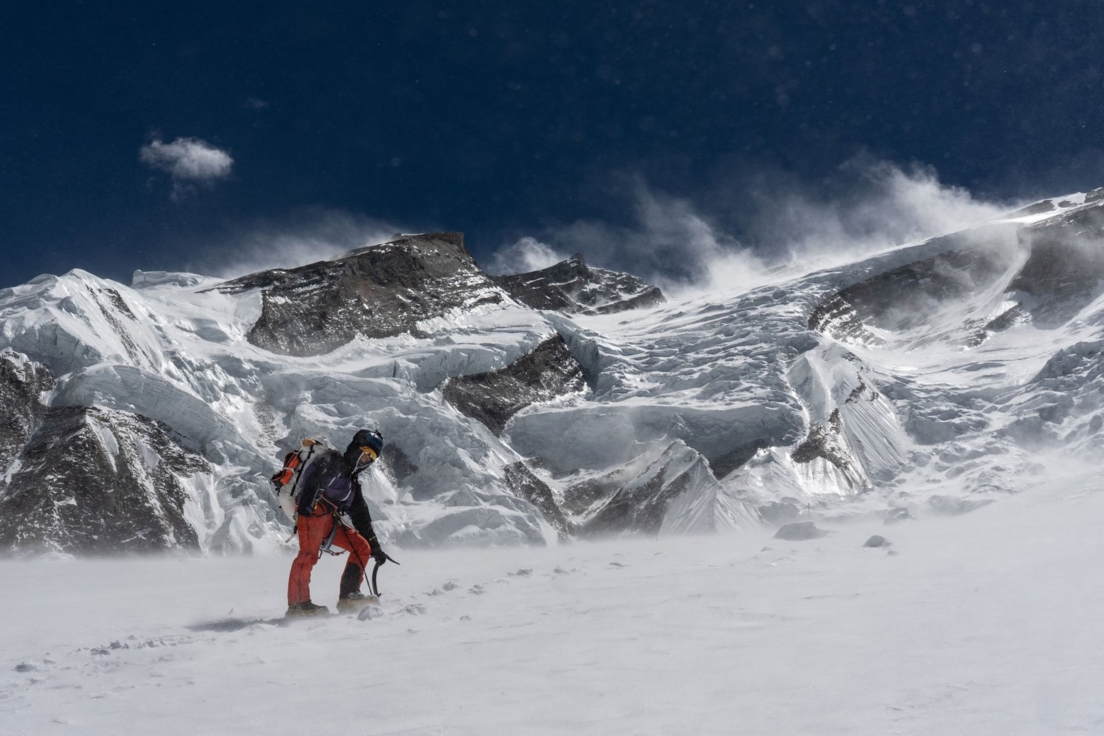 man holding ice axe standing in snow against a mountain