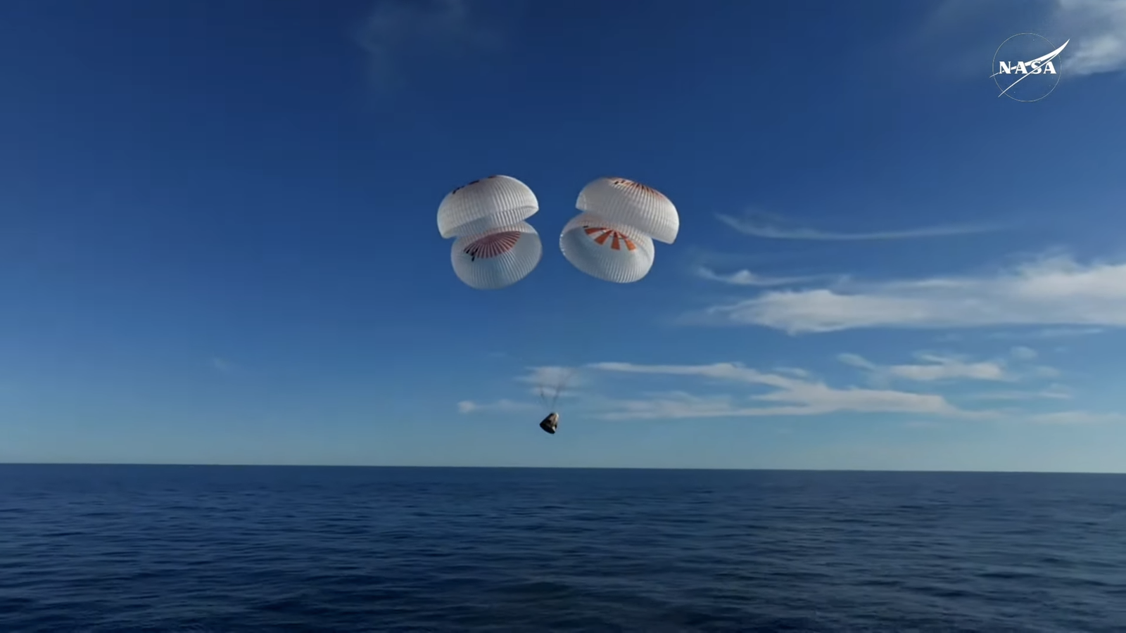 a white space capsule descends toward the ocean under four white and red parachutes