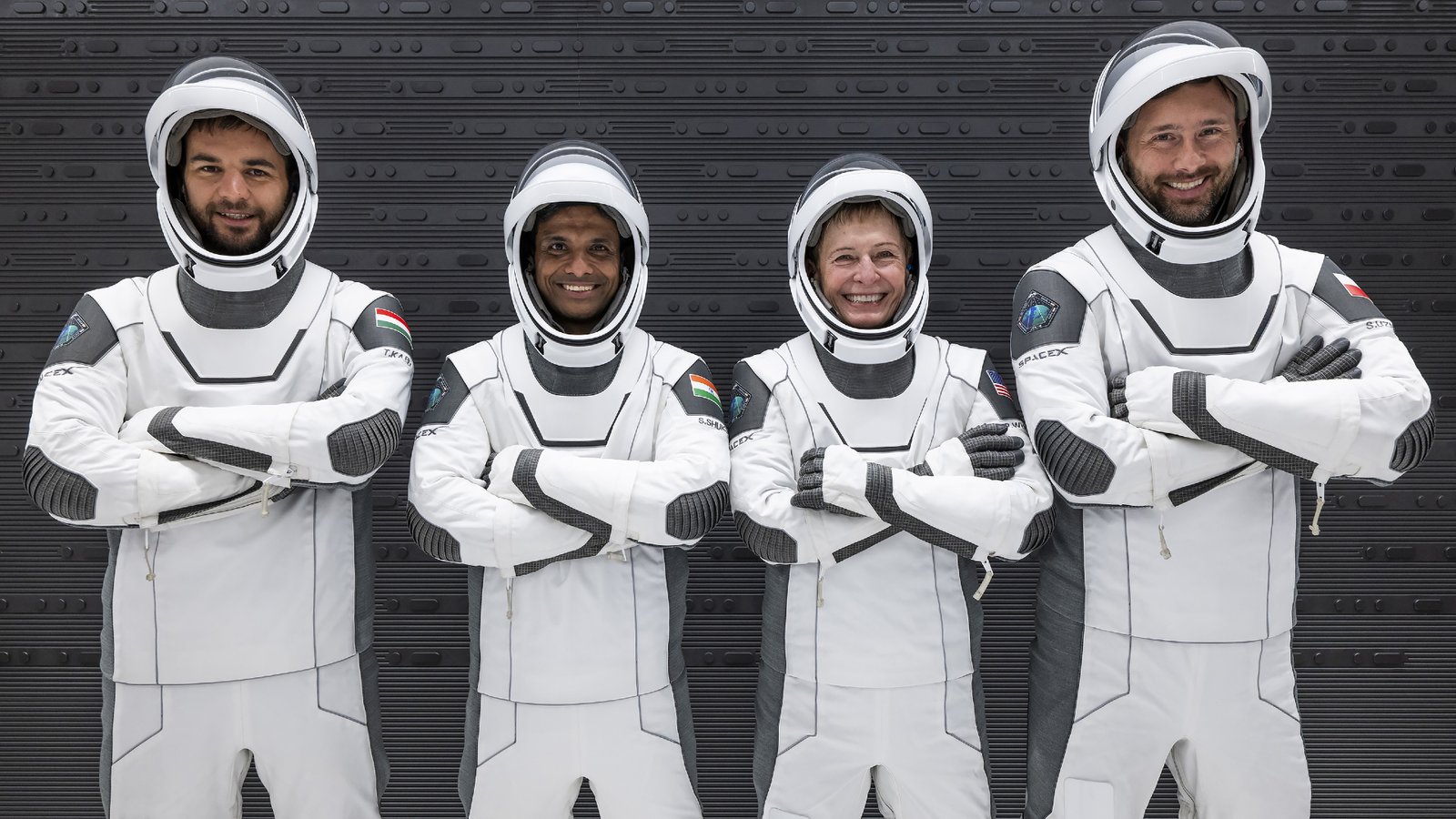 portrait of four astronauts — three men and one woman — in black and white spacesuits