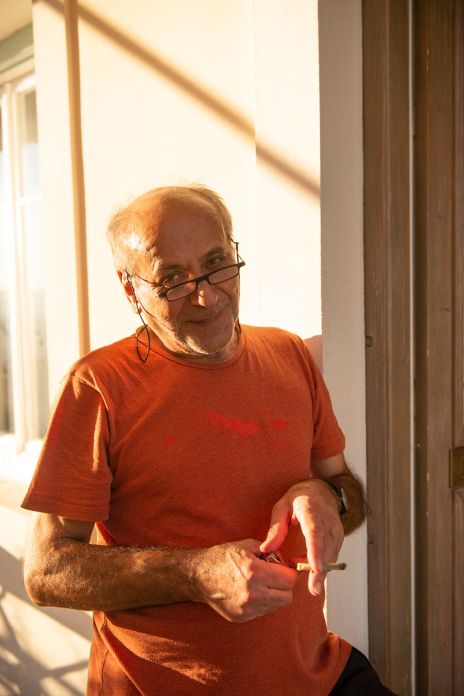 A man smiles gently to camera holding a cigarette