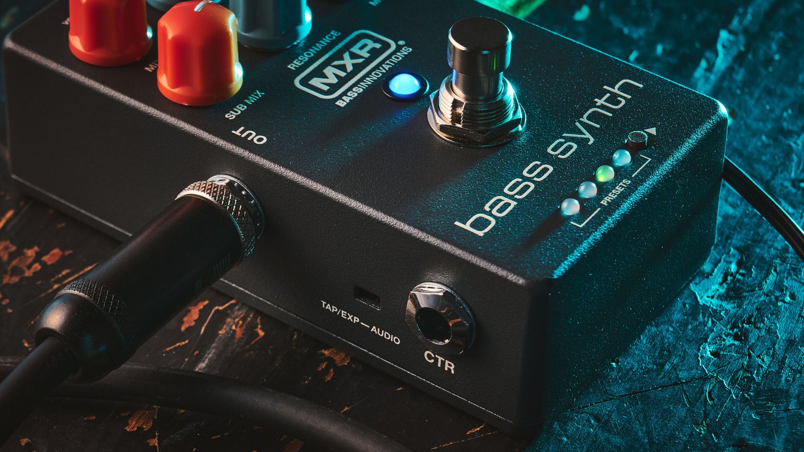 MXR MB301 Bass Synth: the dark gray bass pedal has light blue and orange dials and is photographed here against a distressed wooden background.