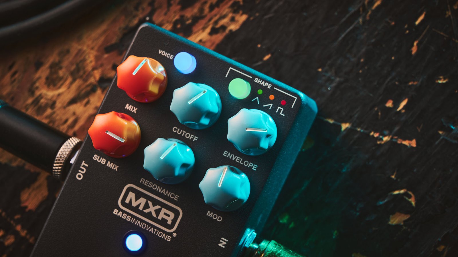 MXR MB301 Bass Synth: the dark gray bass pedal has light blue and orange dials and is photographed here against a distressed wooden background.