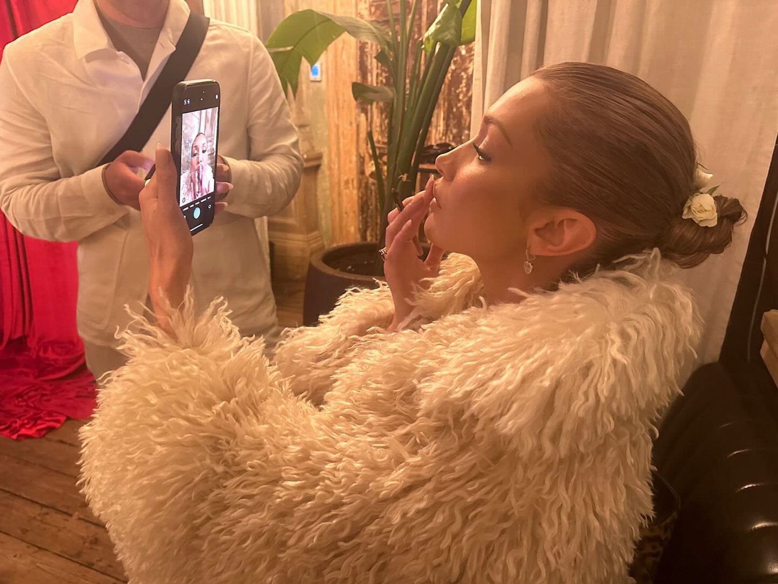 Bella Hadid applies lip liner while looking at a phone. 