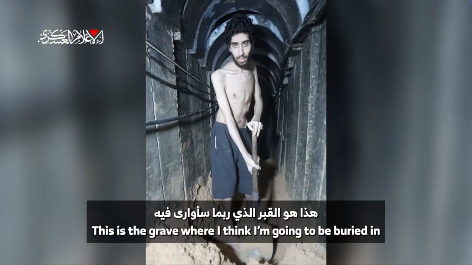Emaciated hostage holding shovel in what appears to be a grave.