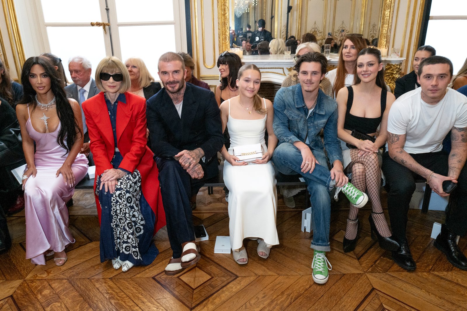 From left, Kim Kardashian in a lilac dress, Anna Wintour in a red coat, sunglasses and blue patterned dress, David Beckham in a black suit and white t-shirt, Harper Beckham in a white dress, Cruz Beckham in a denim jacket and jeans, Nicola Peltz in a black dress, Brooklyn Beckham in a white t-shirt and black pants.