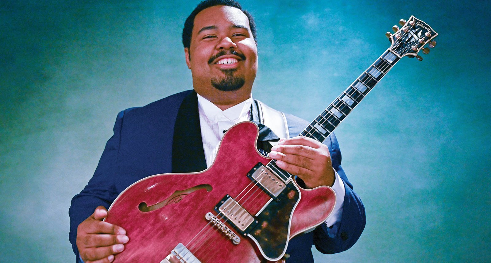 D.K. Harrell poses with his Gibson ES-355 Custom in cherry red against a blue-green background.