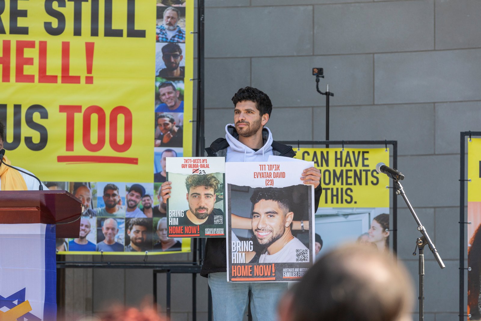 Man holding signs with photos of Israeli hostages at a rally.