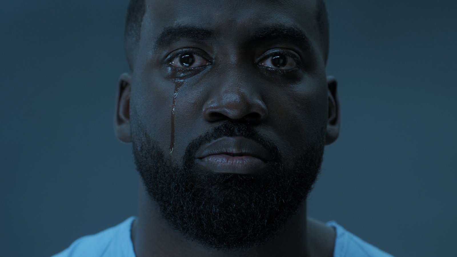 a bearded man stares at us with a tear on his cheek